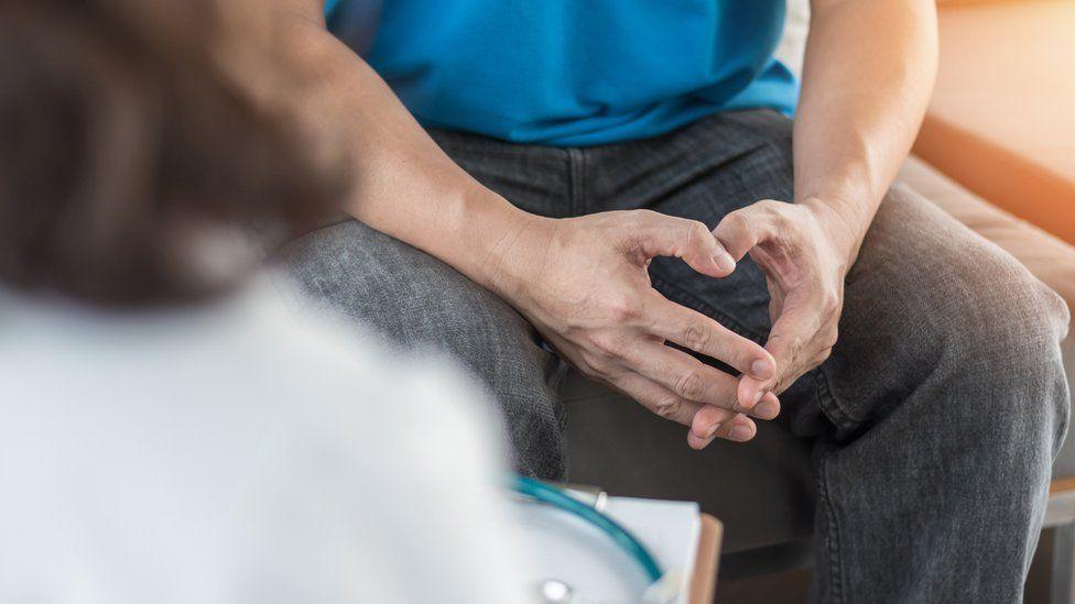 A man with hands crossed on his lap