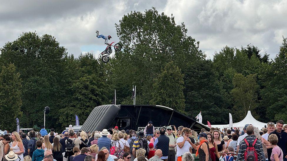 A motorbike stunt rider hangs in mid-air while performing a stunt in front of a large crowd