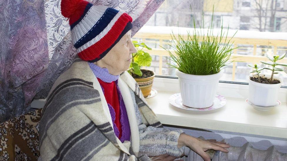 A woman in a hat staying warm by a radiator