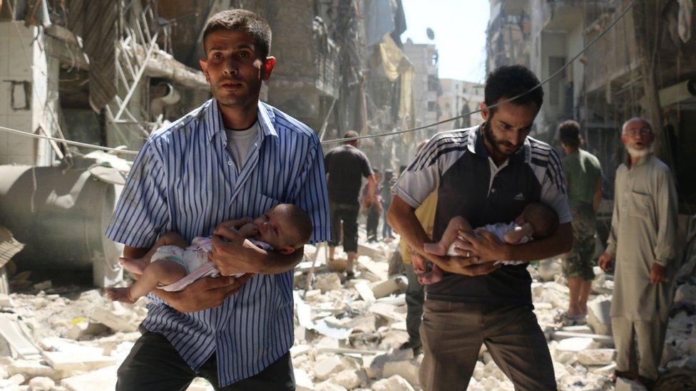 Syrian men carrying babies make their way through the rubble of destroyed buildings following a reported air strike on the rebel-held Salihin neighbourhood of the northern city of Aleppo, on September 11, 2016