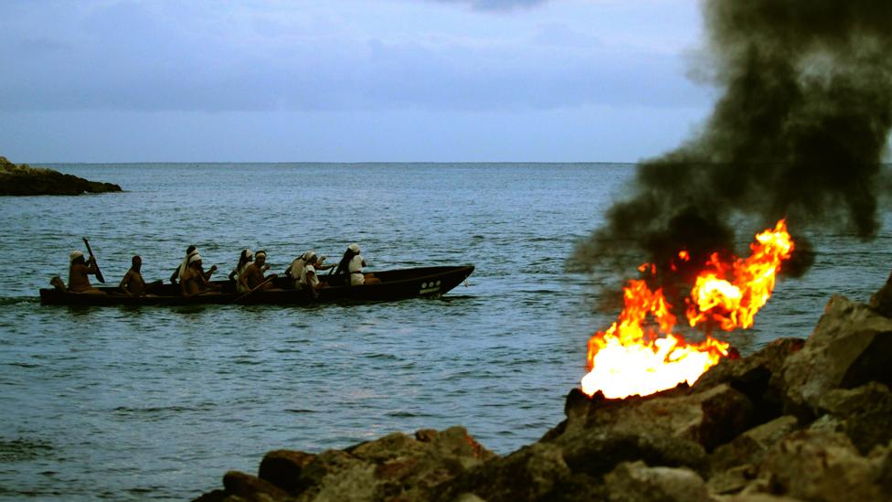 Mayan Indians row in a boat past a fire on the shore as they participate in the ancient ceremony of the 'Mayan Journey' at the ceremonial center of Xcaret