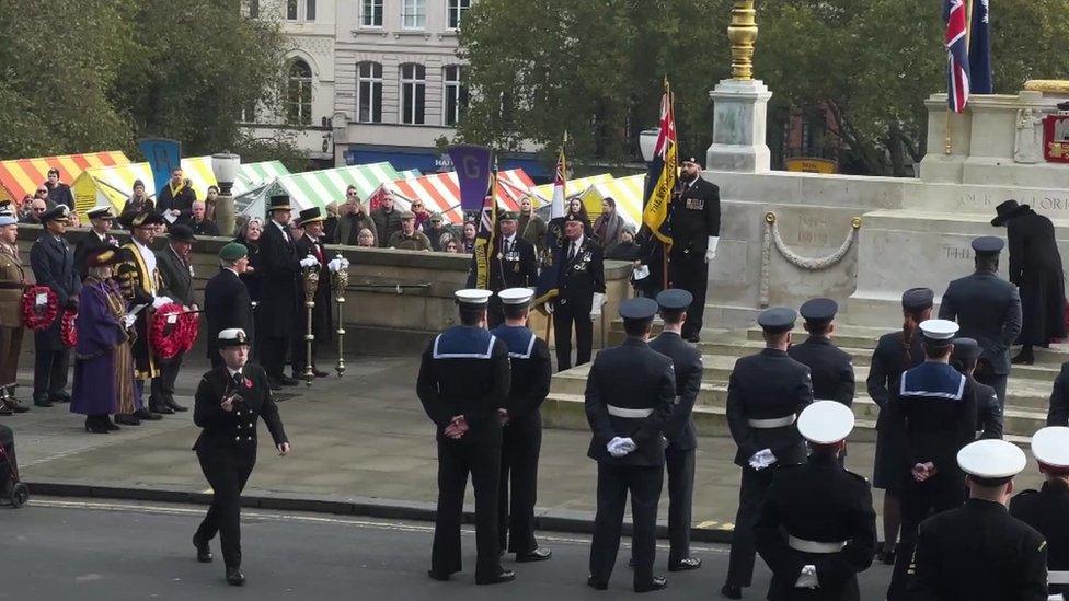 Uniformed personnel assemble by the war memorial in Norwich with the colourful market stalls in the background