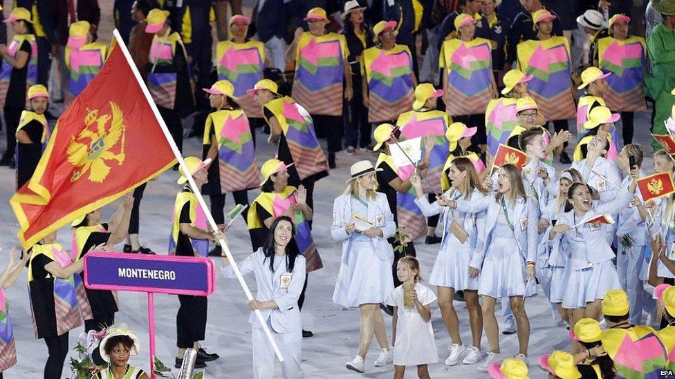 Helpers at the Olympic opening ceremony guide the Montenegro team using brightly coloured ponchos