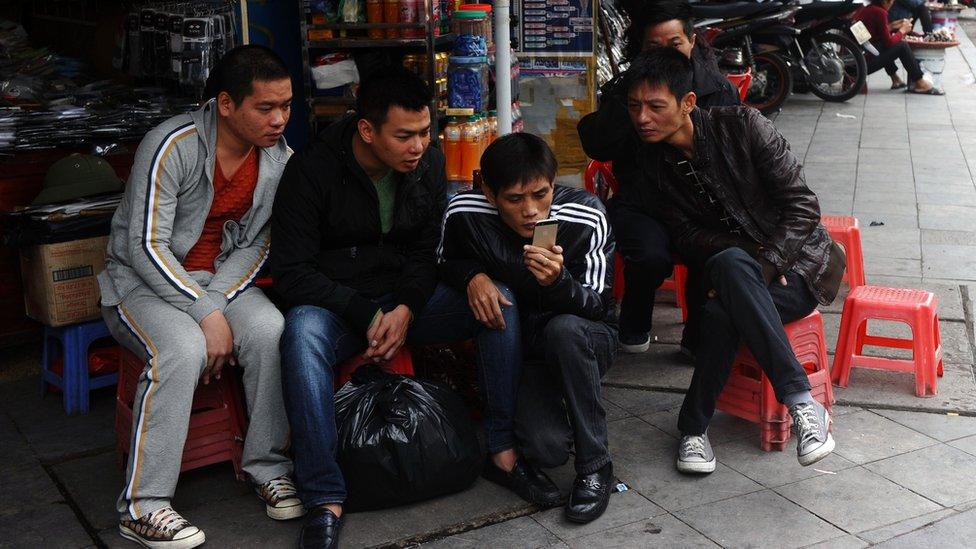 Four men sitting on stools in Vietnam gathered around a single smartphone.