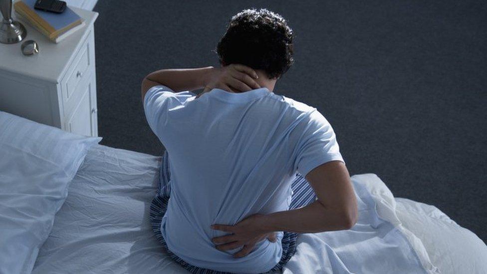 Man holding his back and neck on a bed