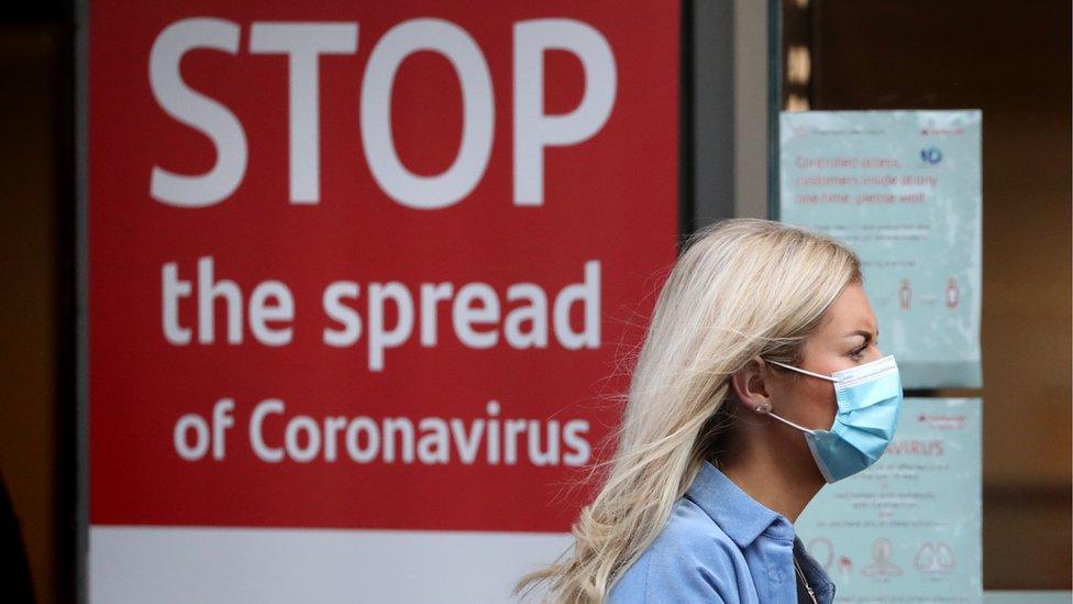 A woman walks past a coronavirus warning sign