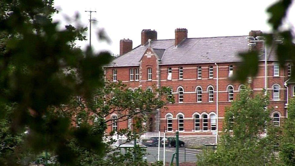 A red bricked building. Trees are in the foreground. Some care are parked beside the building. 