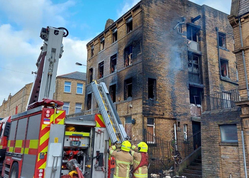 Two firefighters pushing a ladder from a fire engine in front of a burnt out building