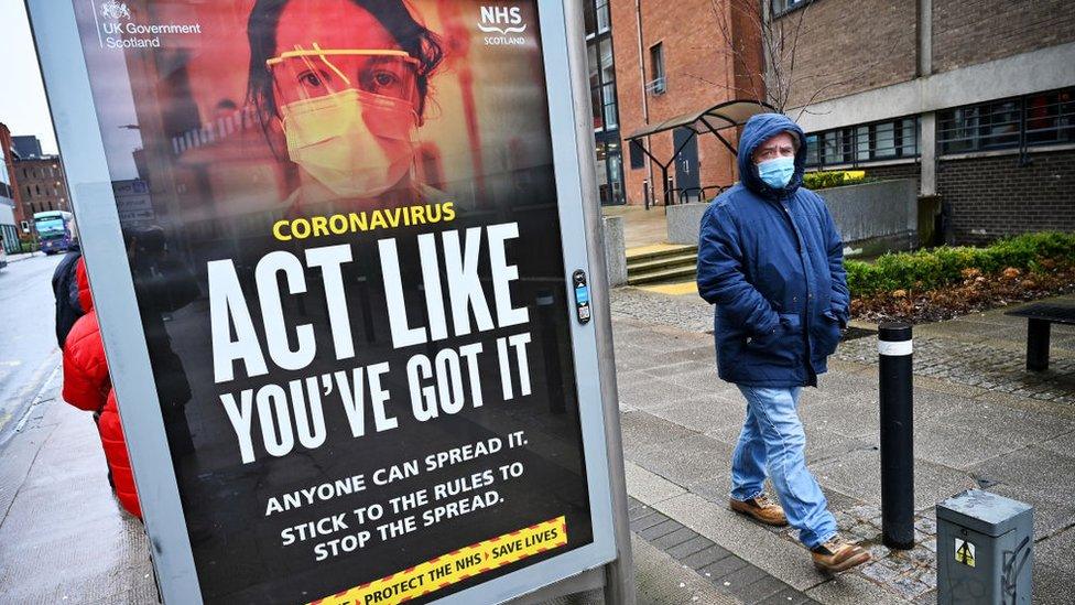 Members of the public walk past a government poster reminding people to socially distance and abide by the lockdown restrictions in the city centre on January 29 2021 in Glasgow