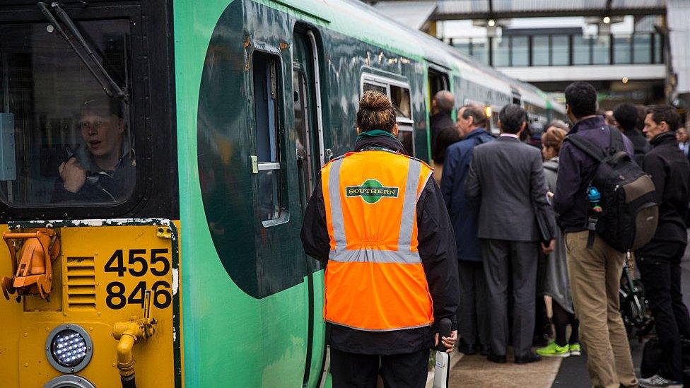 A Southern rail conductor waits as commuters board a train at East Croydon station