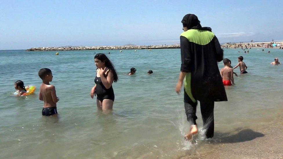 A woman wearing a full-body swimming costume walks into the water at a beach in France (file pic)