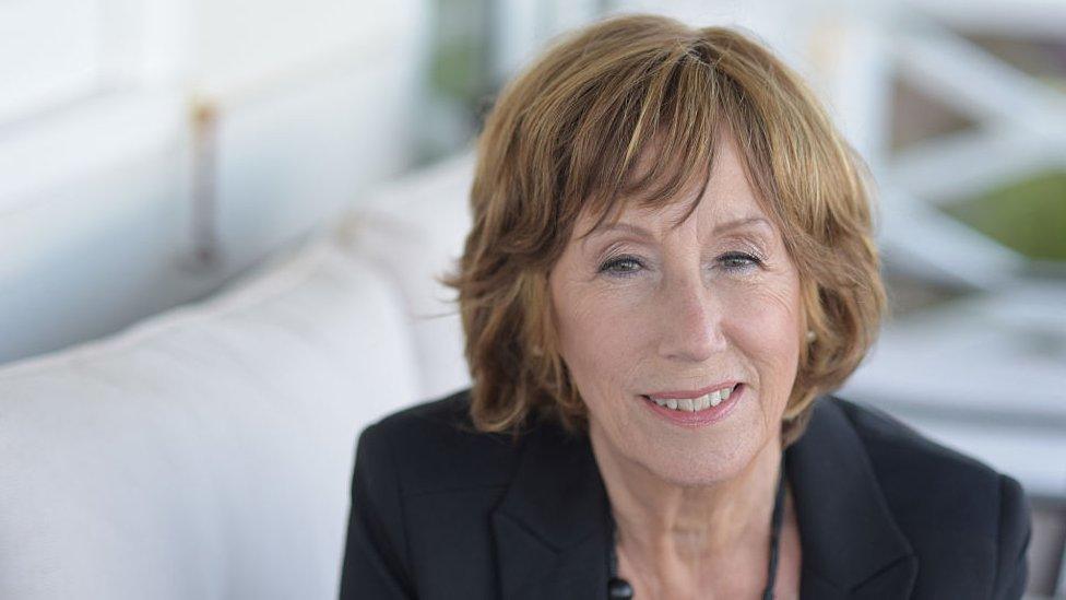 Norma Winstone - an 82-year-old woman with short ginger hair and brown eyes smiles at the camera. She's pictured in a well-lit room, wearing a dark blazer and long black necklace.