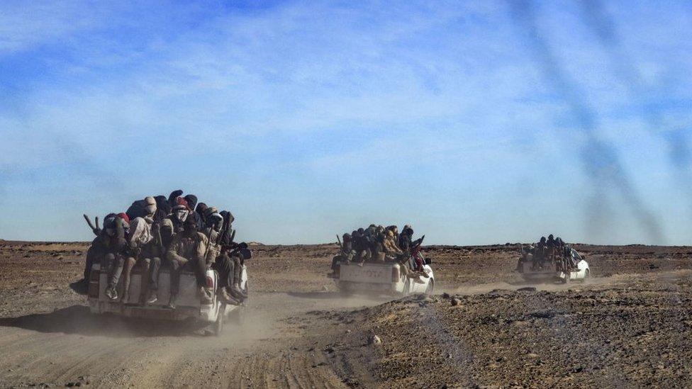 A picture taken from a vehicle and through a window shows a group of migrant men, mainly from Niger and Nigeria, sitting in the back of a pick up, on January 15, 2019 during a journey across the Air dessert, northern Niger, towards the Libyan border post of Gatrone.