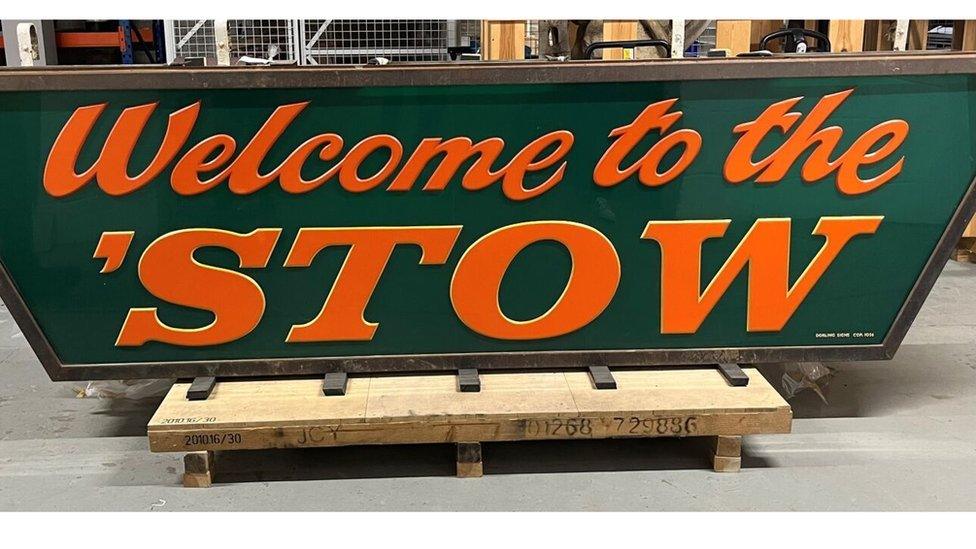 Orange lettering on a green sign that reads "Welcome to the 'Stow"