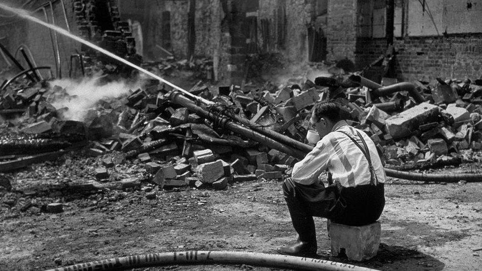 1942: Still wearing his pyjamas, a fireman drinks an early morning cup of tea by the ruins of the shops damaged in the Exeter blitz