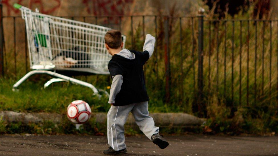 Boy playing football next to abandoned shopping trolley