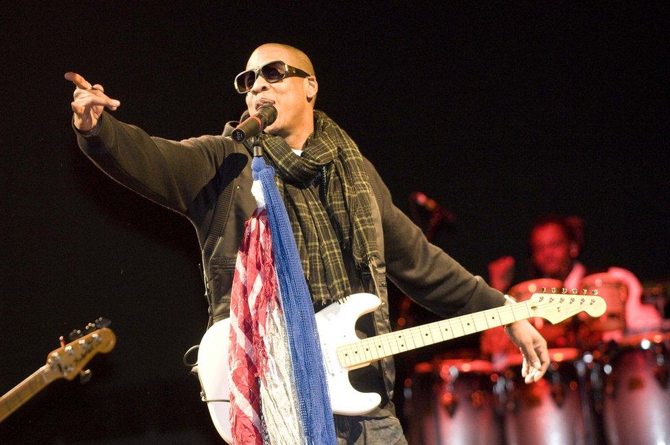 Jay-Z points to the crowd while holding a guitar