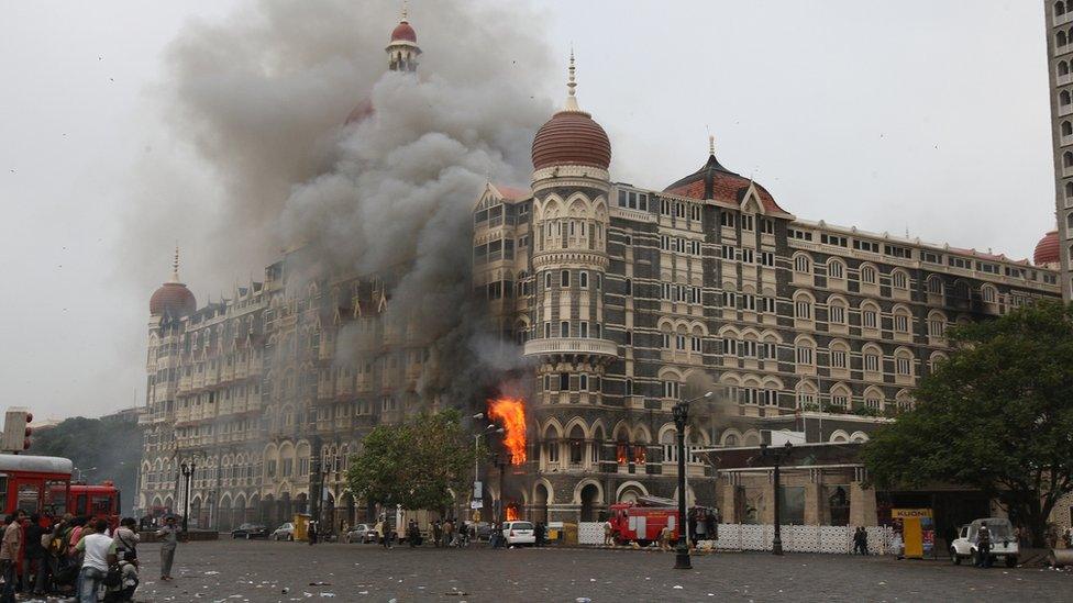 Indian fire brigade officials and bystanders look towards The Taj Mahal hotel in Mumbai on 29 November 2008, as smoke and flames billow out from a section of the building