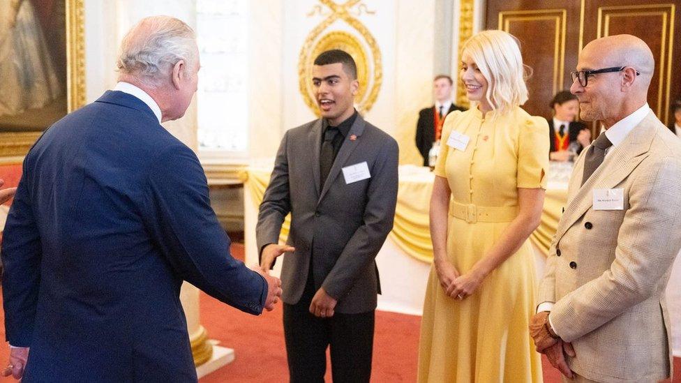 King Charles III shakes hands with Motaz Amer, alongside Holly Willoughby and Stanley Tucci