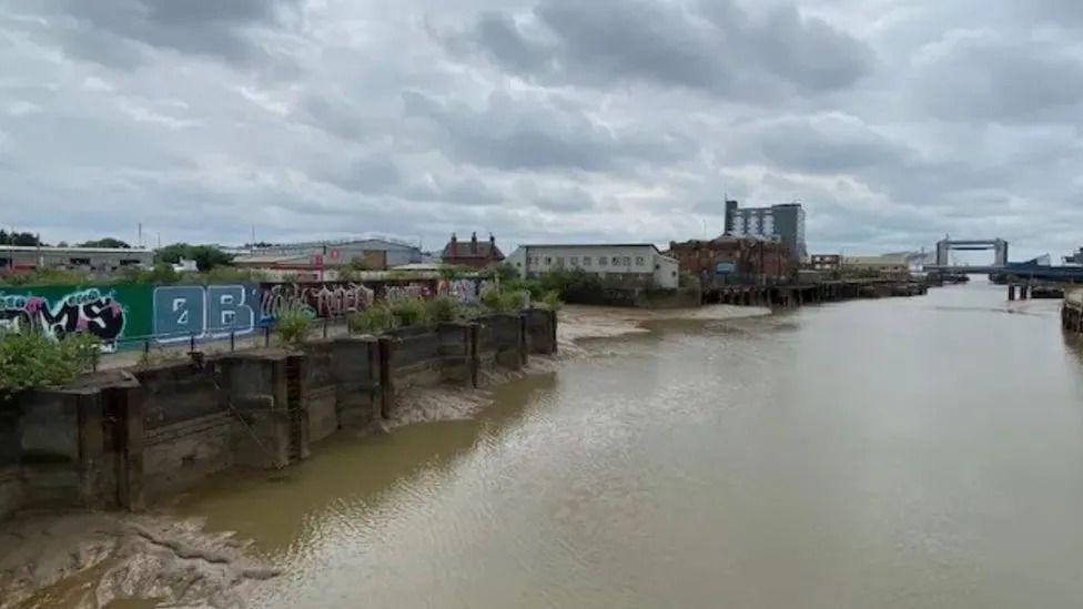 The site next to the River Hull. The river is shown running through the right hand side of the picture. The site is on the left, currently behind a fence covered with graffiti