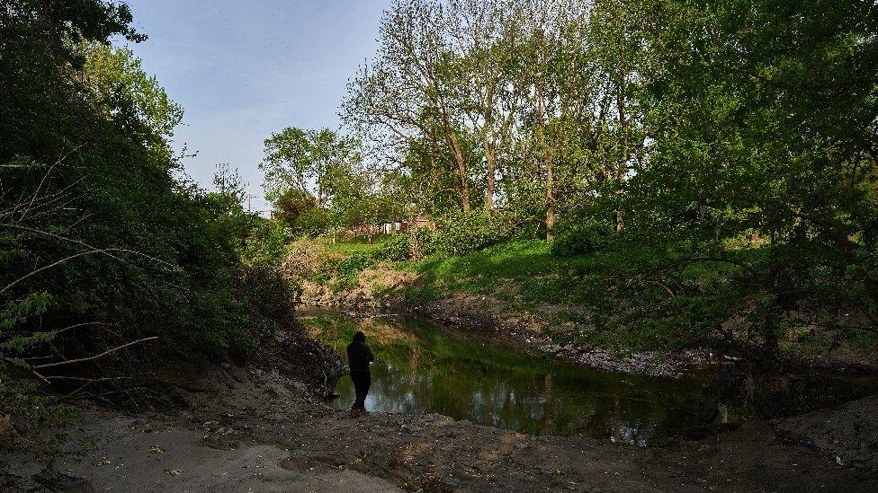 A lone hooded figure stands by the banks of Coldwater Creek