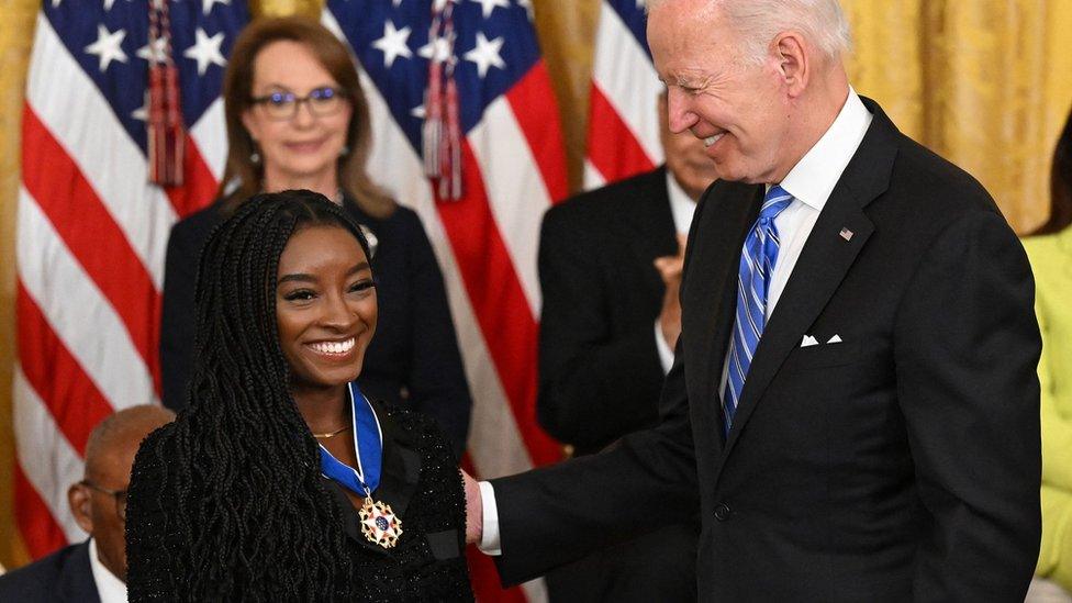 simone biles smiling with medal next to president biden