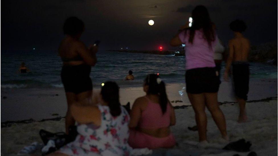 People gather to watch the Strawberry Moon as it rises in Miami Beach, Florida on June 14, 2022.