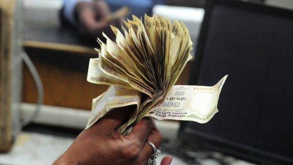 An Indian railway counter cashier waves 500 rupee notes to show that he has no change as passengers use 1000 and 500 rupee notes to purchase rail tickets at Allahabad Railway station in Allahabad on November 9, 2016. I