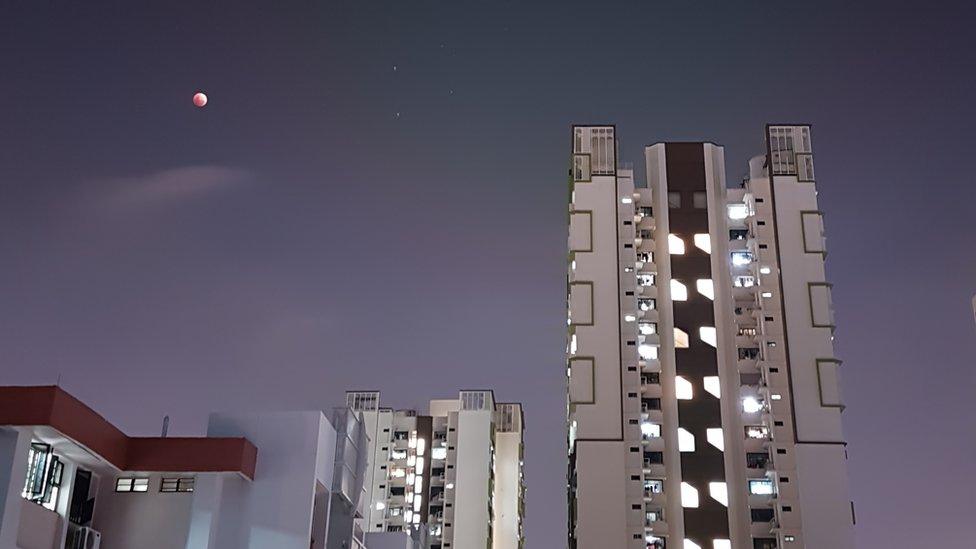 The supermoon is bright red as it appears over a cityscape featuring modern buildings in Singapore.