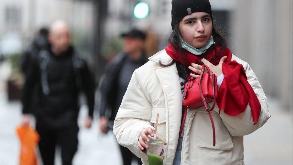 A woman with a mask under her chin walks along a shopping street