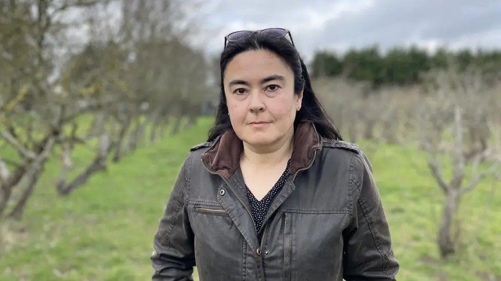 Anna Gazeley in Coton Orchard, Cambridge, with rows of trees behind her