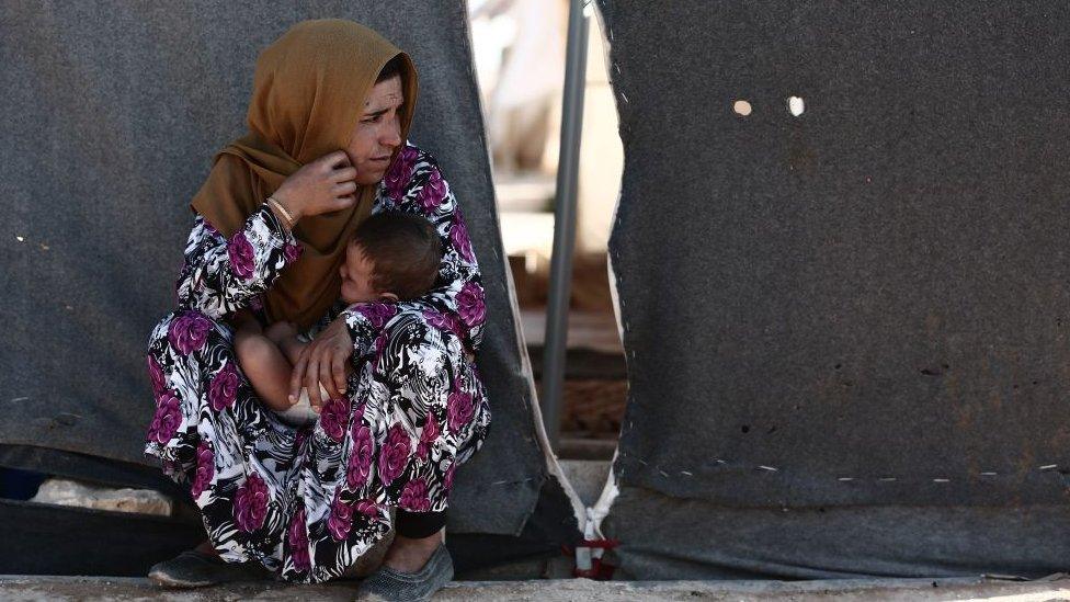 A woman carries a child as she sits in front of a tent at a camp for the displaced from the rebel-held Syrian province of Idlib, at the village of al-Ghadfa