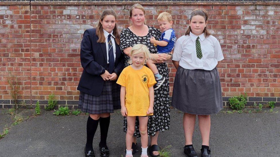 Jodie, pictured with all her four children, shown in front of a red brick wall with modern council-built terraced housing in the background