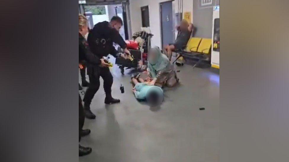 Police officer standing over a man whose face is blurred out lying on the ground 