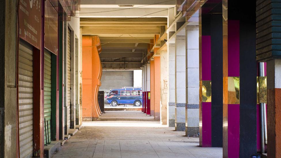 A bus is seen at the end of a long and empty colonnade painted in various colours