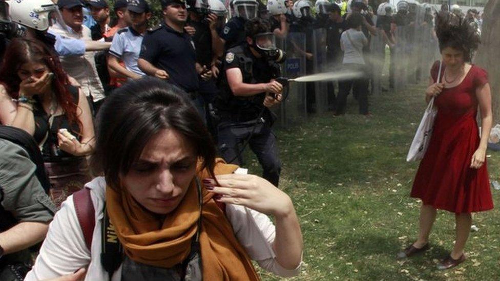 A Turkish riot policeman uses tear gas against Ceyda Sungur (in red dress, right) in Istanbul's Taksim Square in June 2013