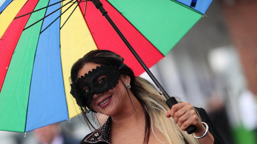 A woman with a face mask holding a brightly coloured umbrella