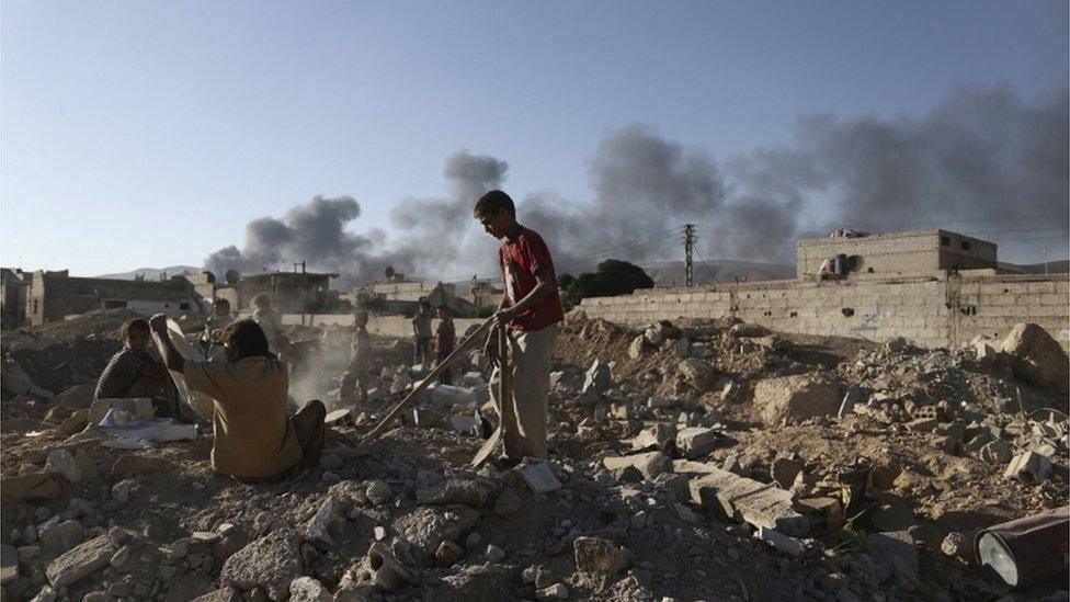 Children inspect rubble as smoke rises behind them during clashes between forces loyal to Syria"s President Bashar al-Assad and the Army of Islam fighters, on the eastern mountains of Qalamoun overlooking the town of Douma, eastern Ghouta in Damascus