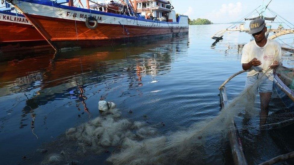 This photo taken on 16 June, 2016 shows a fisherman fixing a net next to the fishing fleet at the port in Masinloc in Zambales province.