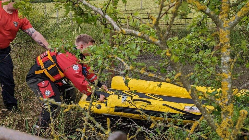 Two firefighters push a yellow raft out on to the muddy pond