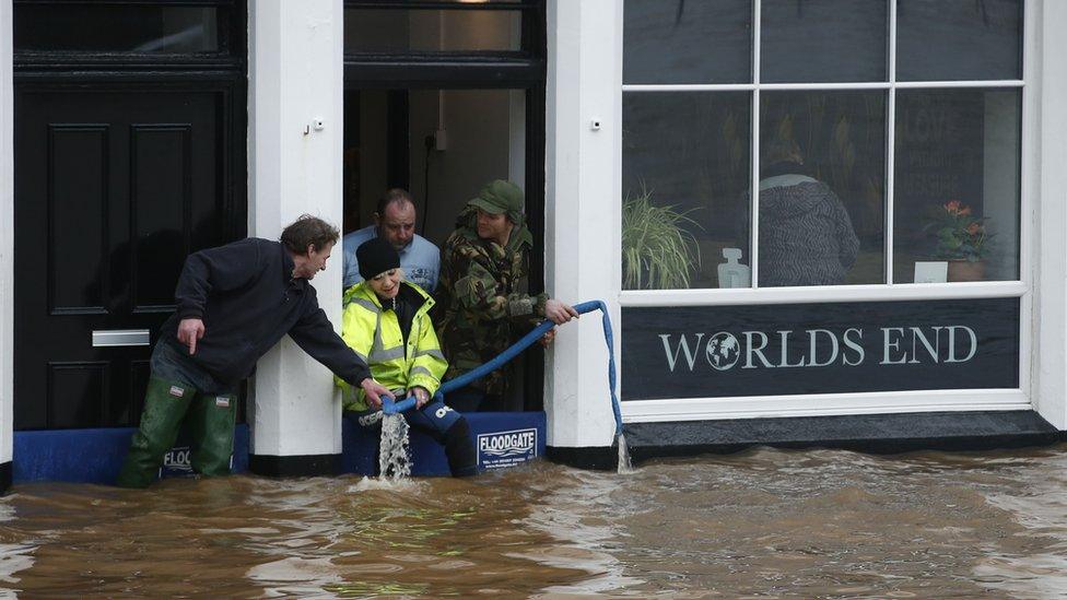 People pumping water from the door of a pub, with floodwater outside