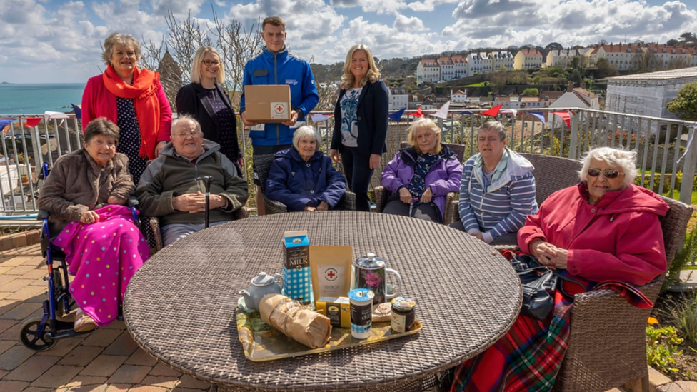 Elderly people sat round a table with the contents of a hamper on the table