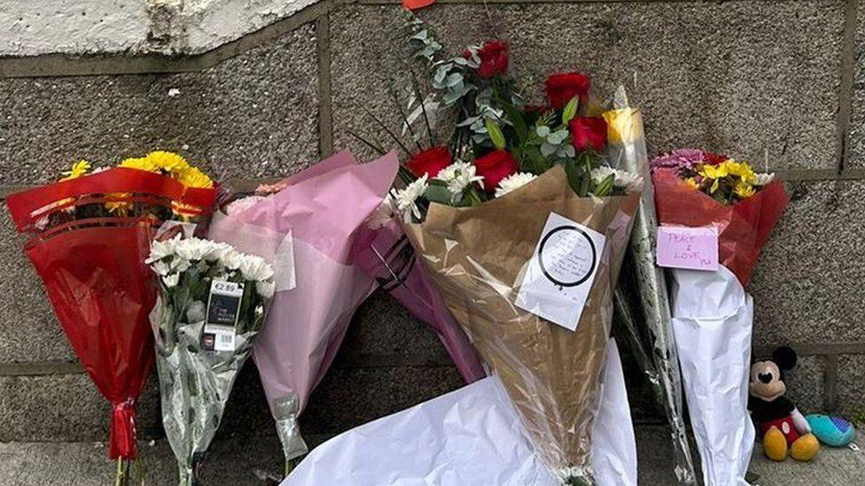 Bouquets of flowers with messages lie on the ground. There is also a Micky Mouse teddy.