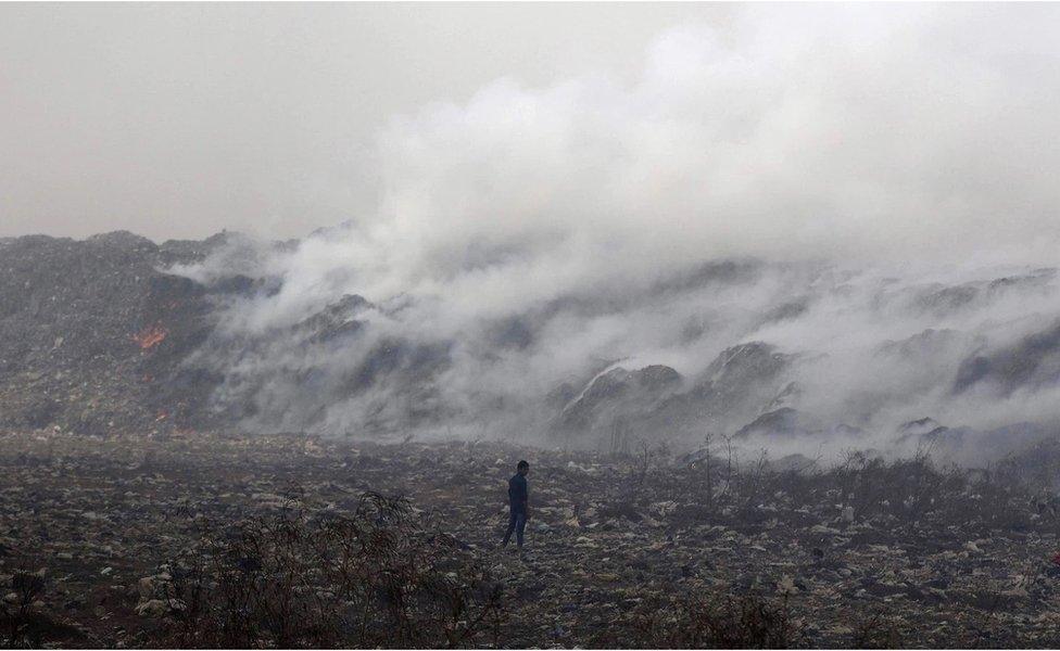 A boy stands amid garbage as smoke billows from the burning Deonar dumping ground in Mumbai in March 2016