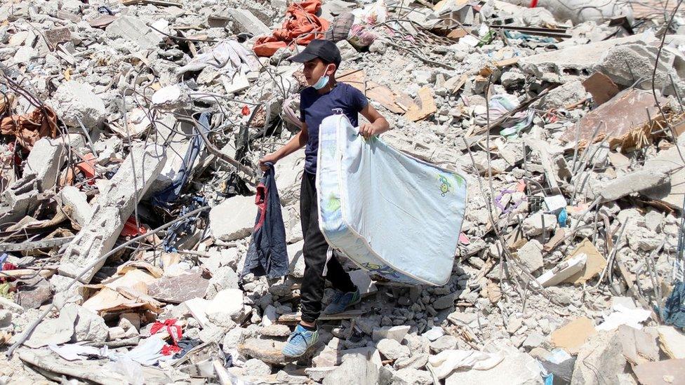 A Palestinian boy carries a mattress as he walks over the rubble of destroyed buildings in Gaza City (2 June 2021)