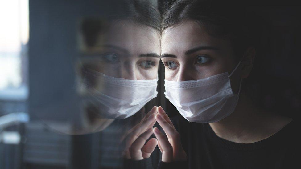 Woman in surgical mask looking out of a window