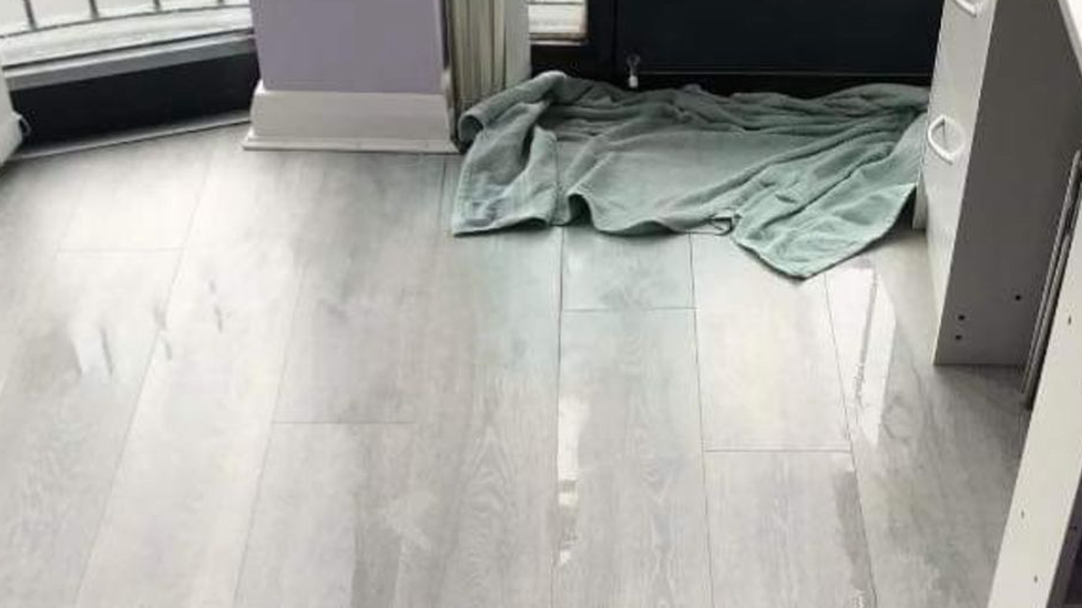 A towel on a wet floor where water has entered through gaps in doors in a house in Killaire Wood