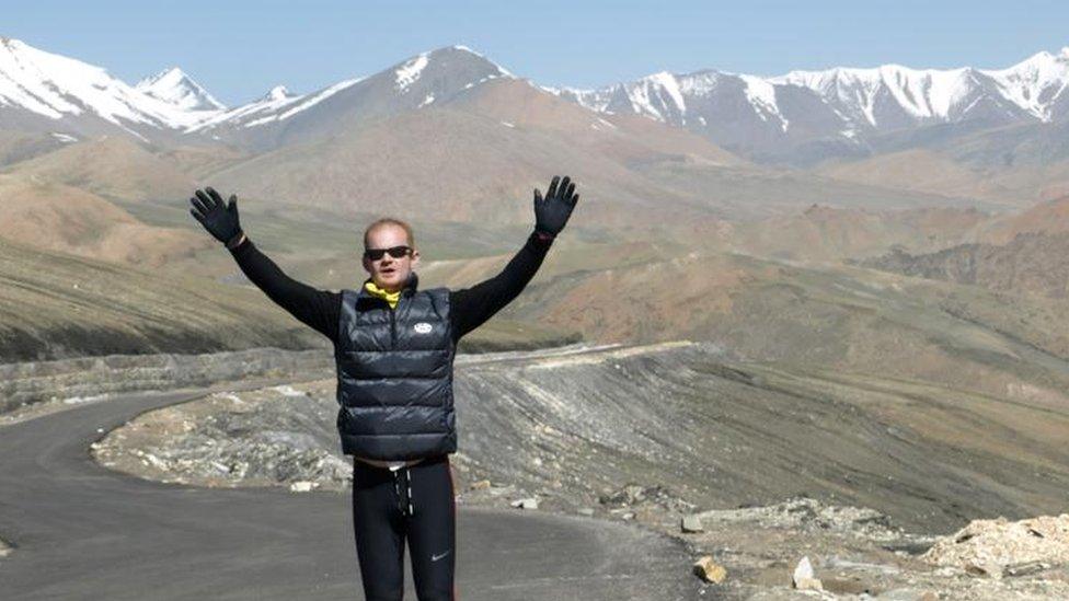 A man standing with his arms raised by a mountain