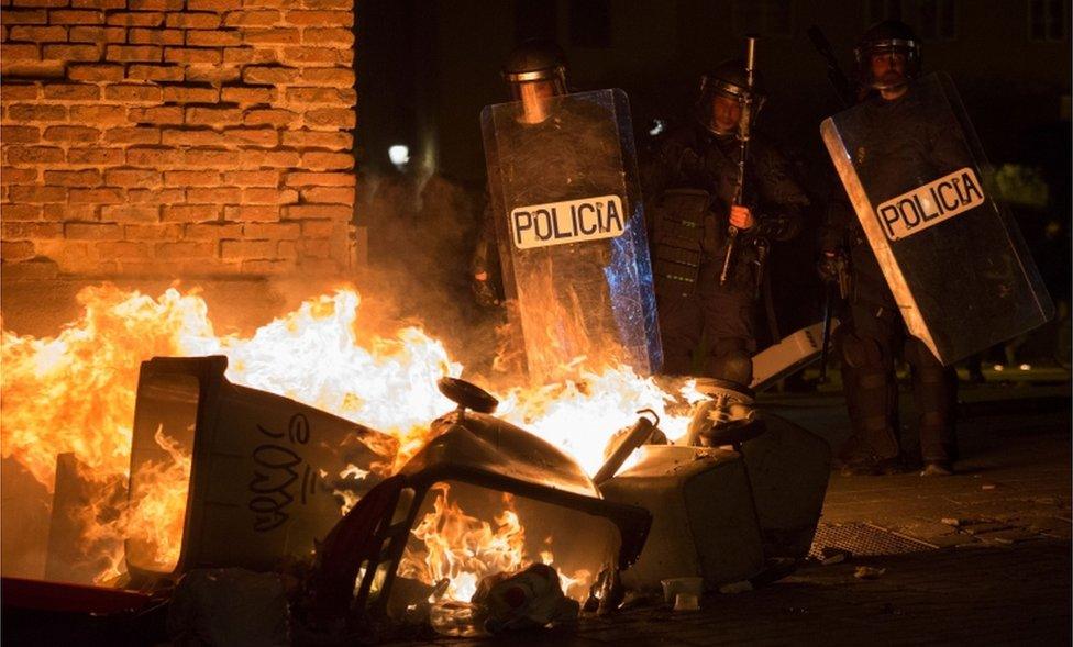 Spanish police officers stand close to burning bins in Madrid's Lavapies district