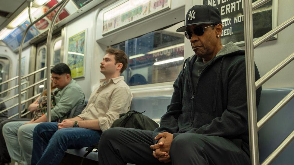 Denzel Washington in dark glasses and a baseball cap on the New York subway in a still from Highest 2 Lowest